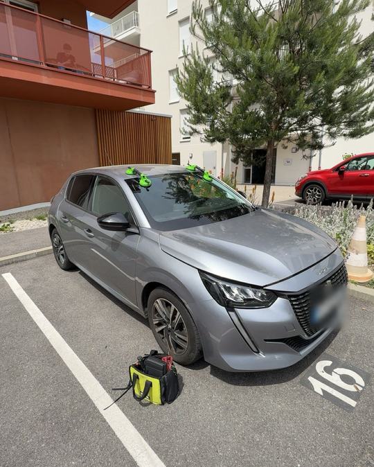 Peugeot 208 grise avec pare-brise neuf maintenu par des ventouses