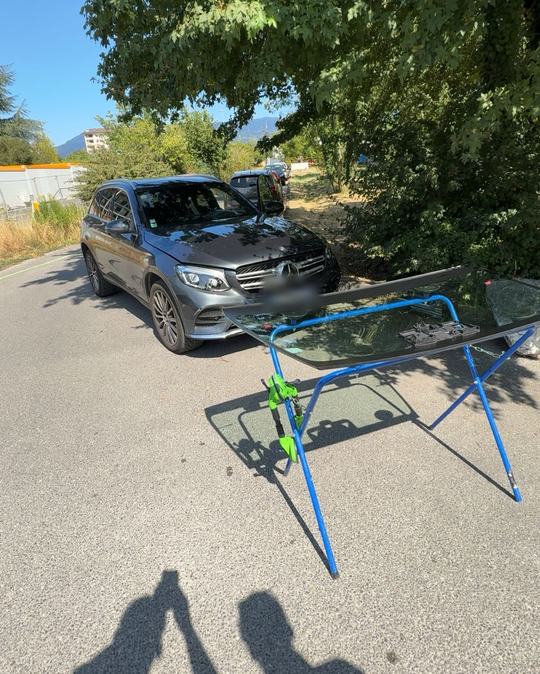 Mercedes GLC gris et pare-brise neuf sur chevalet, sous les arbres