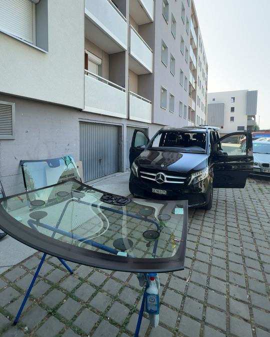 Pare-brise neuf posé sur chevalet devant un van Mercedes noir