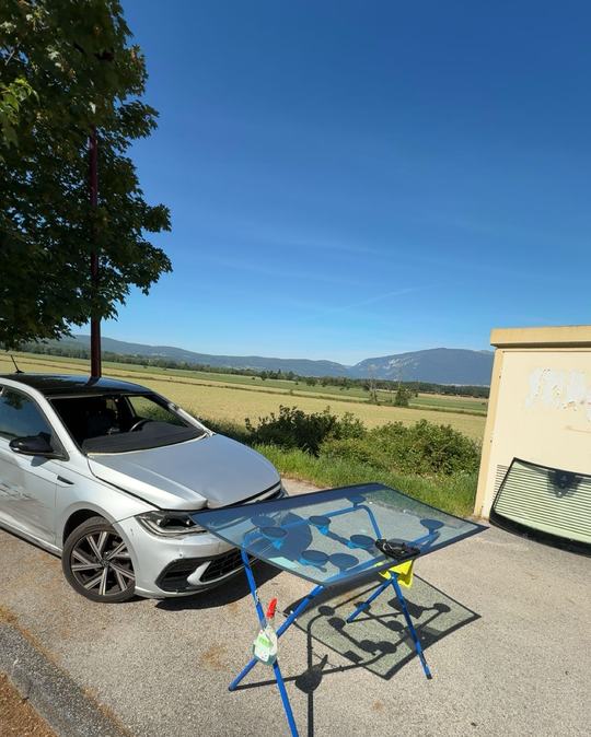 Volkswagen Polo blanche et pare-brise neuf sur chevalet, au milieu des champs